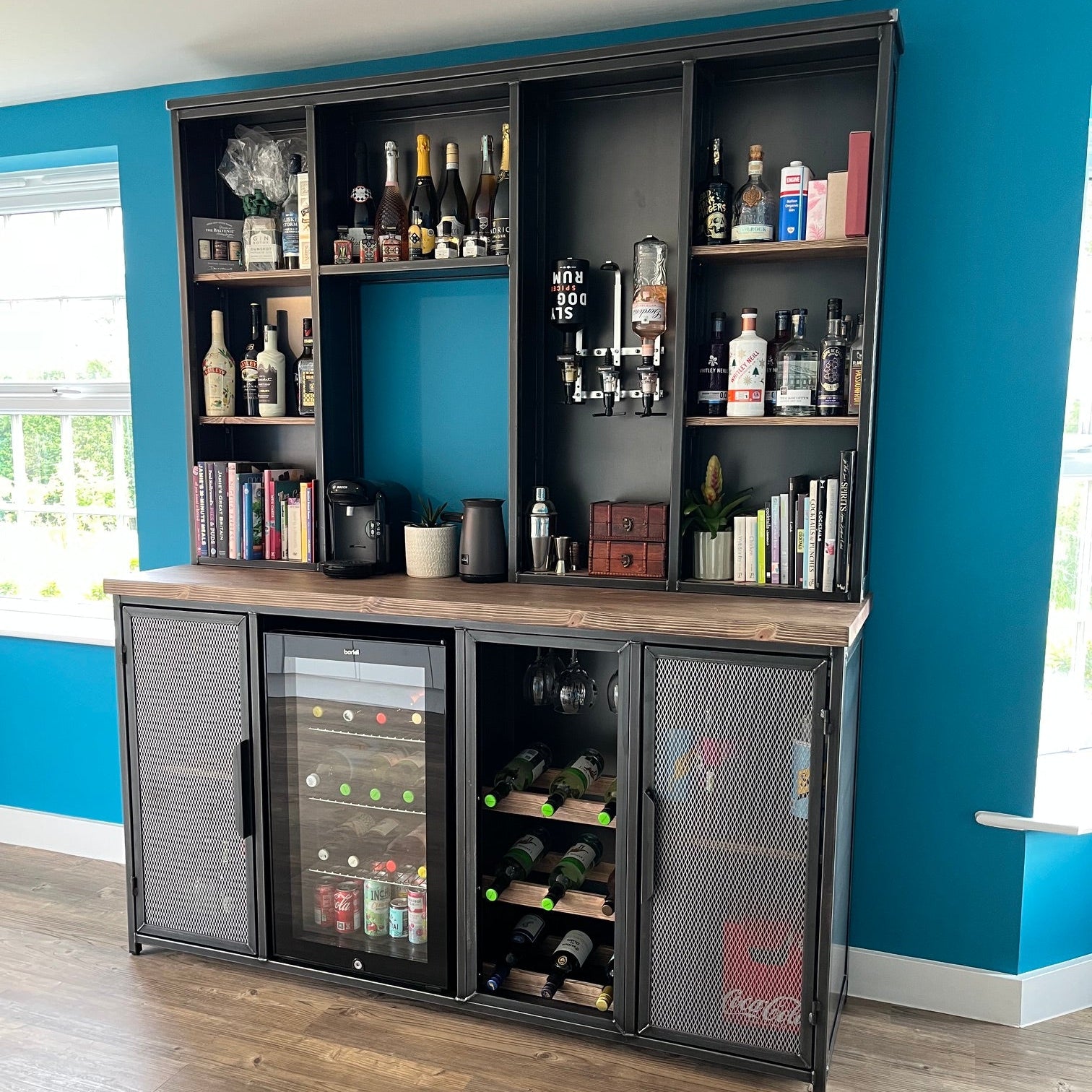 A tall black metal bar and wine storage cabinet with multiple shelves, a countertop, and a glass-front refrigerator, shown in a room with blue walls and wood flooring.