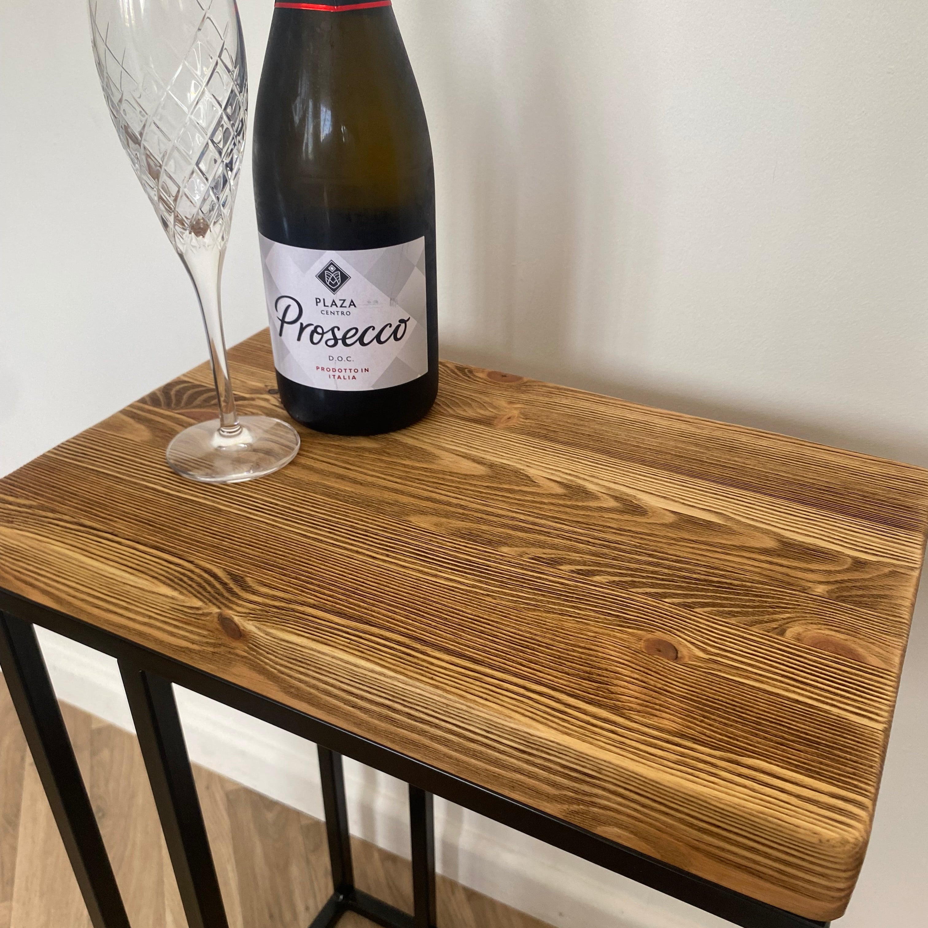 Close-up of a rustic wooden C-shaped side table with a bottle of Prosecco and a crystal champagne flute on top