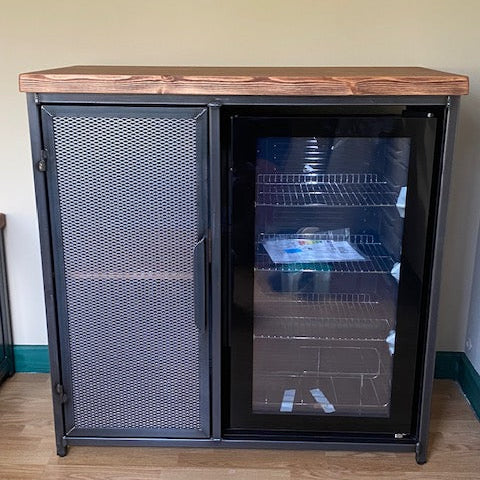 metal fridge cabinet with a rustic wood top, featuring a solid mesh door on the left and a glass-door refrigerator compartment on the right, shown in an indoor room setting.