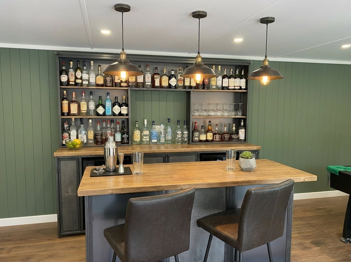 Bar area with wooden counter, chairs, and shelves stocked with bottles against a green wall.